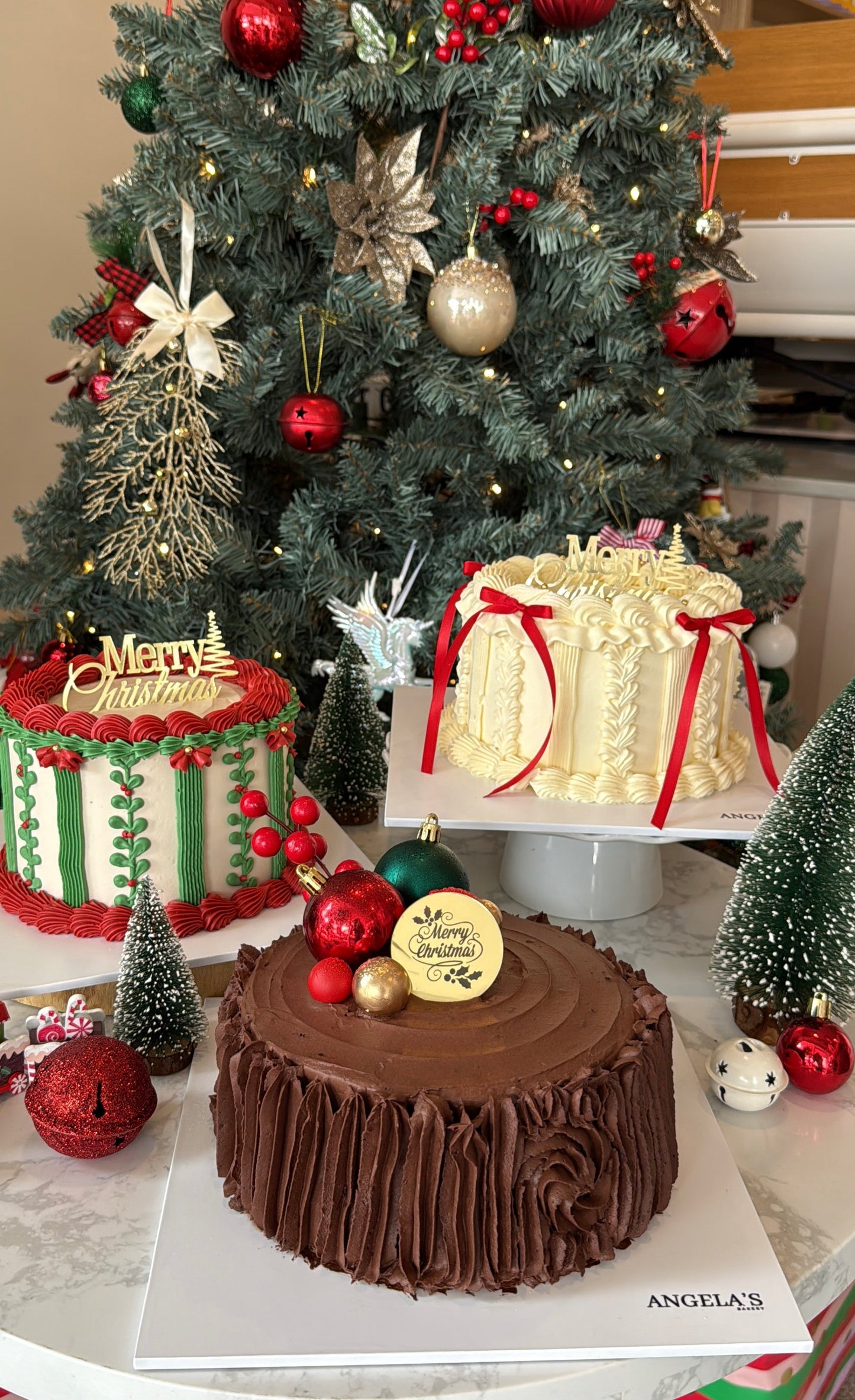 Decorative cakes with Christmas-themed decorations in front of a Christmas tree.